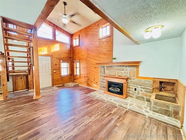 unfurnished living room featuring a textured ceiling, wood finished floors, wood walls, a fireplace, and ceiling fan