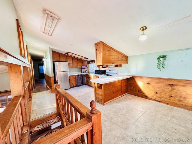 kitchen with freestanding refrigerator, a peninsula, brown cabinetry, lofted ceiling, and white range with gas stovetop