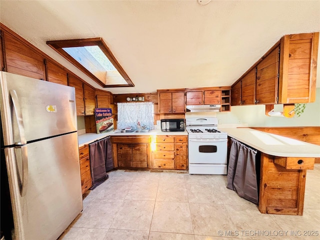 kitchen with brown cabinets, a sink, gas range gas stove, freestanding refrigerator, and black microwave