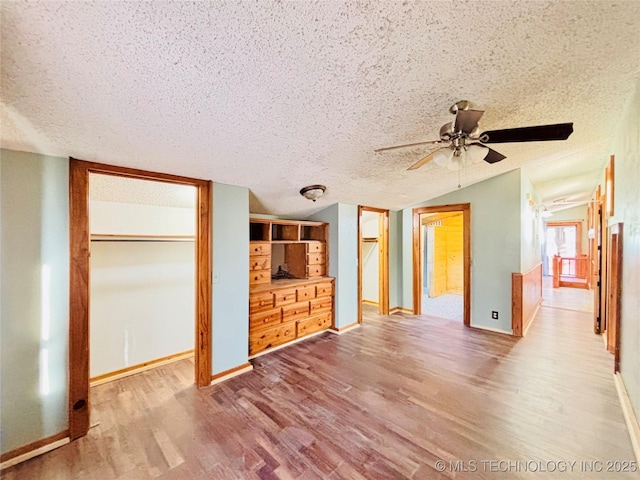 unfurnished bedroom featuring wood finished floors, baseboards, lofted ceiling, a textured ceiling, and two closets