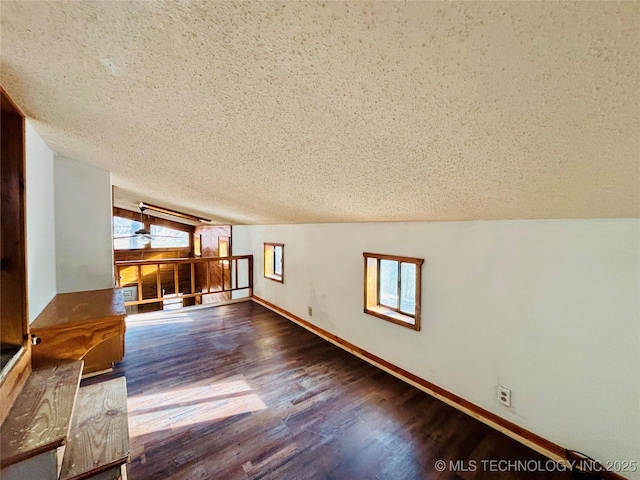 interior space with lofted ceiling, wood finished floors, baseboards, and a textured ceiling