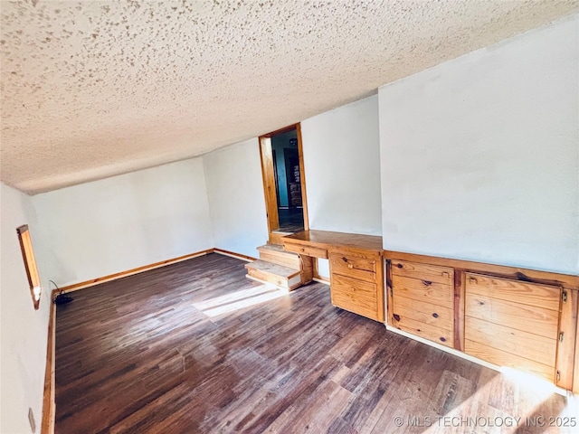 spare room with wood finished floors, baseboards, built in study area, vaulted ceiling, and a textured ceiling