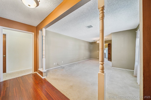 below grade area featuring visible vents, a textured ceiling, baseboards, and wood finished floors