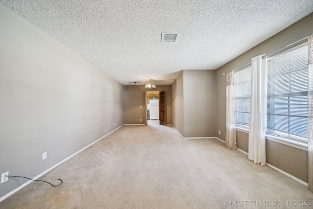 spare room featuring a textured ceiling, baseboards, visible vents, and light carpet