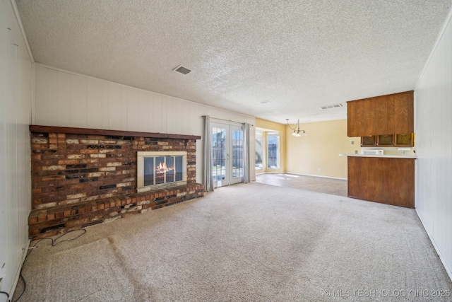 unfurnished living room featuring a brick fireplace, visible vents, carpet floors, and a textured ceiling