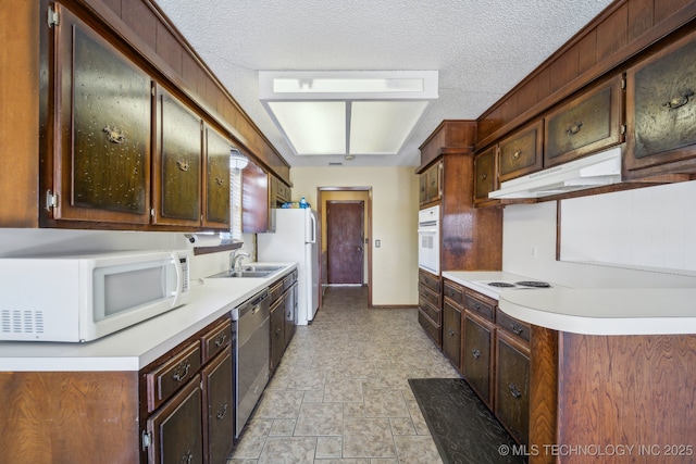 kitchen featuring white appliances, a sink, light countertops, stone finish floor, and under cabinet range hood