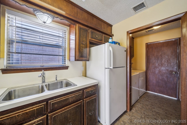 kitchen featuring visible vents, freestanding refrigerator, a sink, a textured ceiling, and washing machine and dryer