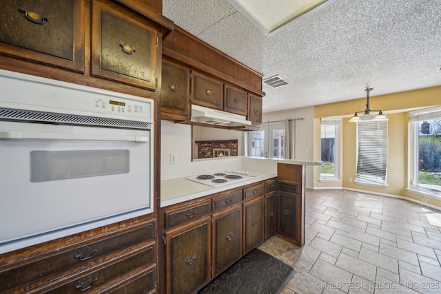 kitchen featuring visible vents, under cabinet range hood, a textured ceiling, white appliances, and light countertops