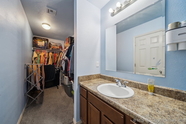 bathroom featuring visible vents, a walk in closet, and vanity