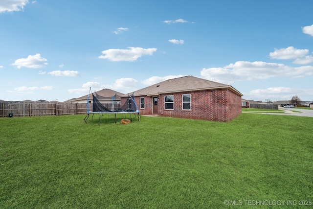 rear view of house featuring brick siding, a trampoline, a lawn, and fence