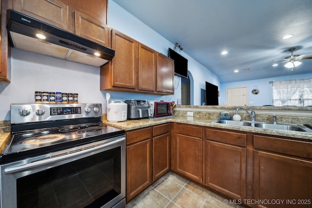 kitchen featuring stainless steel electric range oven, ceiling fan, a sink, under cabinet range hood, and brown cabinets