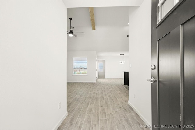 hallway with light wood-type flooring, baseboards, beamed ceiling, and a towering ceiling