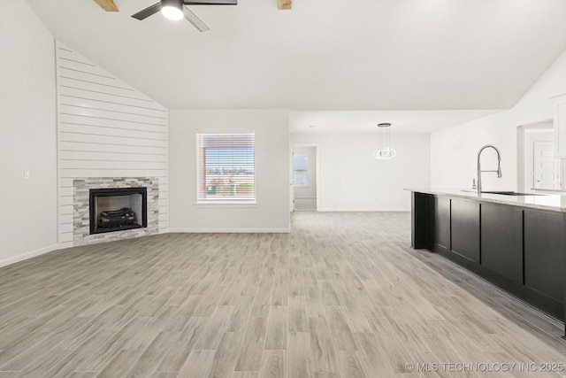 unfurnished living room with a large fireplace, ceiling fan, vaulted ceiling, light wood-style flooring, and a sink