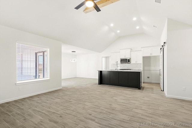 kitchen featuring a ceiling fan, light wood finished floors, white cabinets, stainless steel microwave, and open floor plan