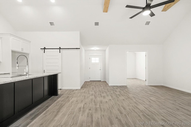 unfurnished living room with a sink, a barn door, light wood-style floors, and a ceiling fan