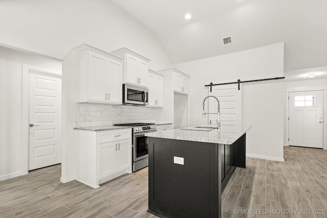 kitchen featuring wood finish floors, white cabinetry, stainless steel appliances, a barn door, and lofted ceiling