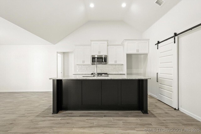 kitchen featuring stainless steel microwave, white cabinets, a barn door, and visible vents