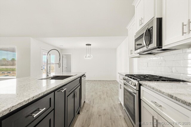 kitchen featuring light wood-style flooring, a sink, stainless steel appliances, white cabinets, and backsplash