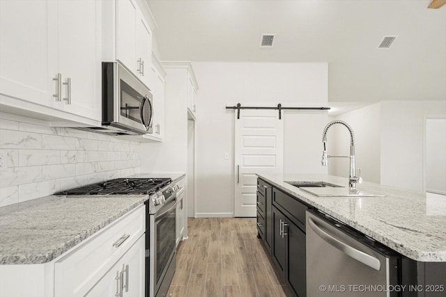 kitchen with a sink, stainless steel appliances, white cabinets, a barn door, and tasteful backsplash