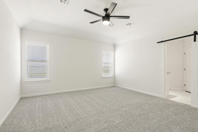 spare room with a wealth of natural light, a barn door, light colored carpet, and ceiling fan