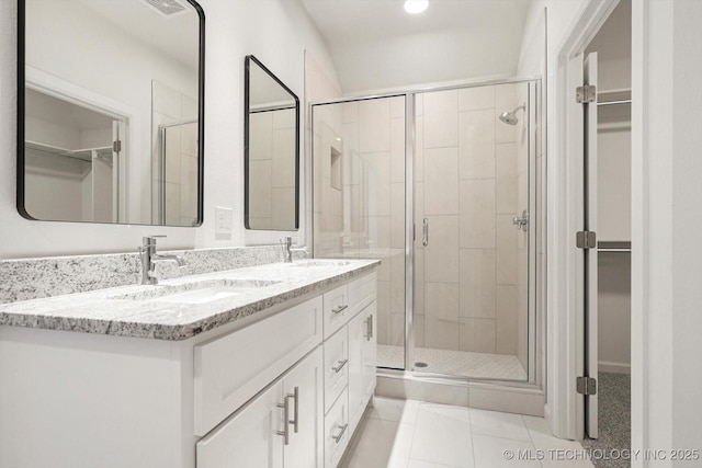 full bath featuring a walk in closet, a stall shower, tile patterned flooring, and a sink