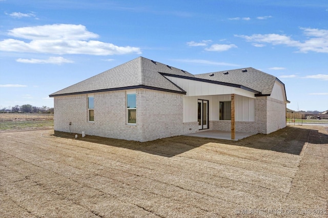 back of house with brick siding, a patio area, and roof with shingles