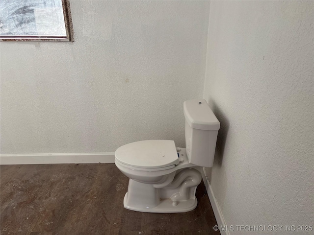 bathroom with toilet, a textured wall, and baseboards