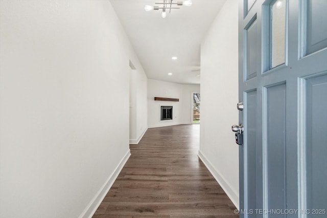 corridor with dark wood-type flooring, recessed lighting, baseboards, and a chandelier