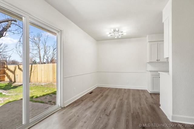 unfurnished dining area with an inviting chandelier, baseboards, and light wood-style floors