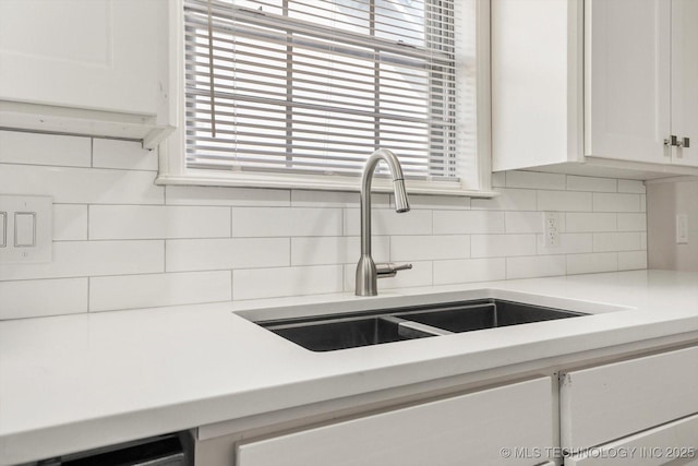 kitchen with tasteful backsplash, white cabinetry, light countertops, and a sink