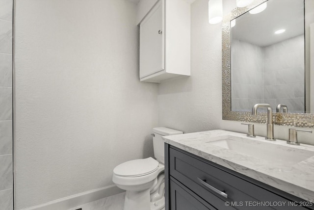 bathroom featuring toilet, vanity, baseboards, and a textured wall