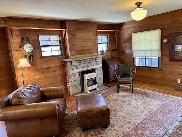 living room featuring wooden walls, a stone fireplace, and wood finished floors