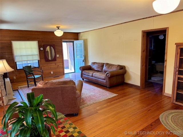 living room featuring baseboards, wood walls, and light wood finished floors