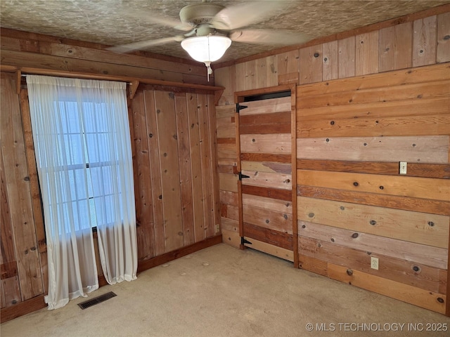 spare room featuring wooden walls, a ceiling fan, visible vents, and light carpet