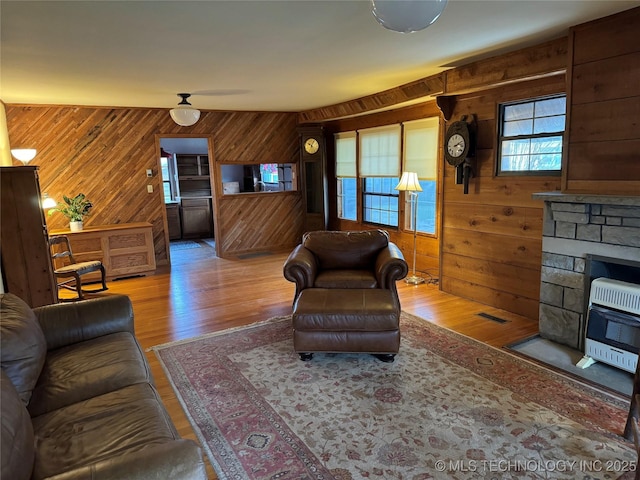 living room with a stone fireplace, wooden walls, heating unit, and wood finished floors