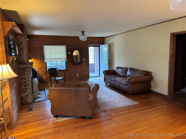 living area with visible vents, a fireplace, light wood-type flooring, and wooden walls