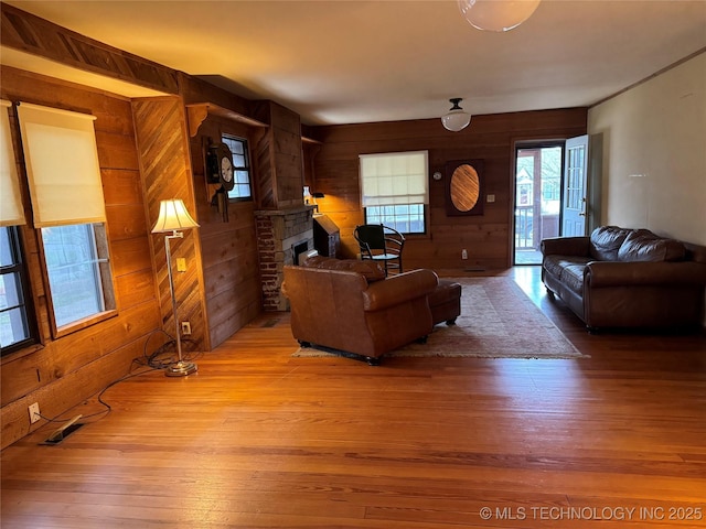 living area featuring light wood finished floors, wooden walls, a brick fireplace, and visible vents