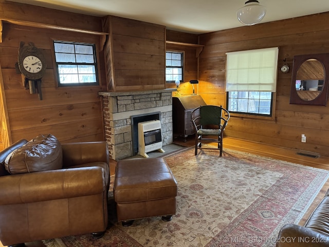 707 E 15th St, Okmulgee, OK 74447 - living room featuring heating unit, wood walls, a stone fireplace, and wood finished floors