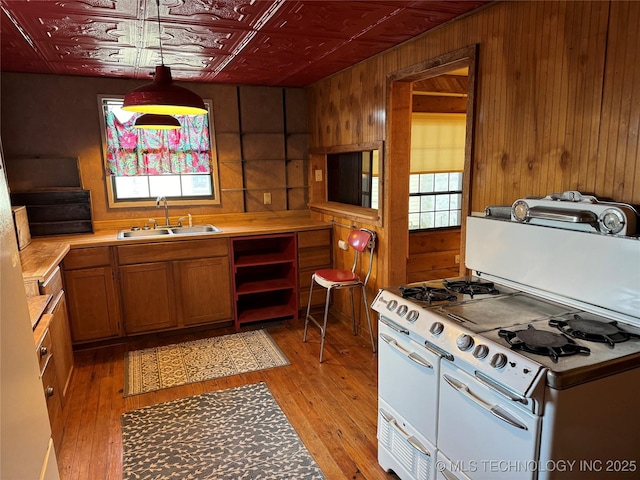 kitchen featuring brown cabinets, a sink, double oven range, an ornate ceiling, and wooden walls