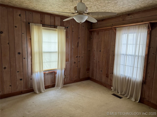 empty room featuring visible vents, light colored carpet, wood walls, and ceiling fan