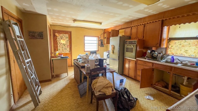 kitchen with a sink, brown cabinets, freestanding refrigerator, and oven