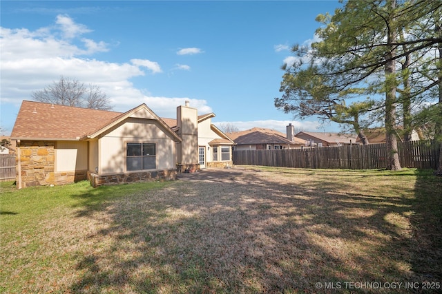 rear view of property with a yard, a fenced backyard, stone siding, and a chimney