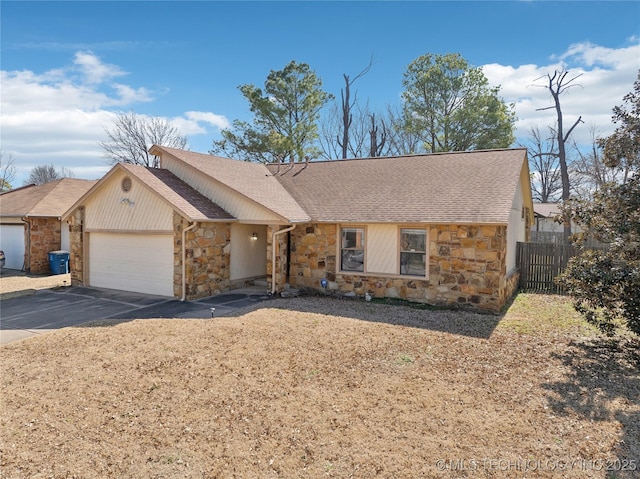 view of front facade featuring fence, a shingled roof, a garage, stone siding, and aphalt driveway