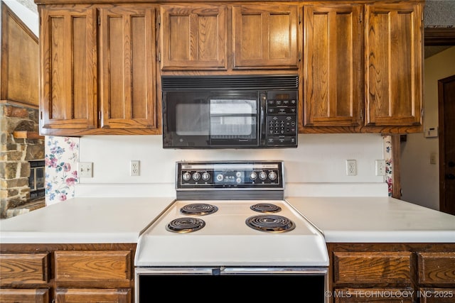 kitchen featuring brown cabinetry, light countertops, electric range oven, and black microwave