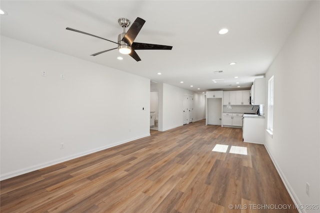 unfurnished living room with wood finished floors, baseboards, recessed lighting, a sink, and ceiling fan