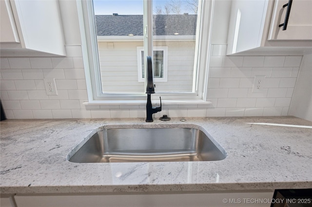 details with backsplash, light stone countertops, white cabinetry, and a sink