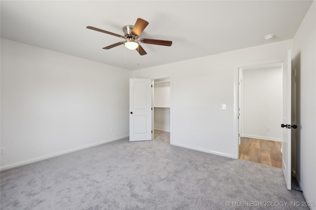 unfurnished bedroom featuring a walk in closet, baseboards, a ceiling fan, and carpet flooring