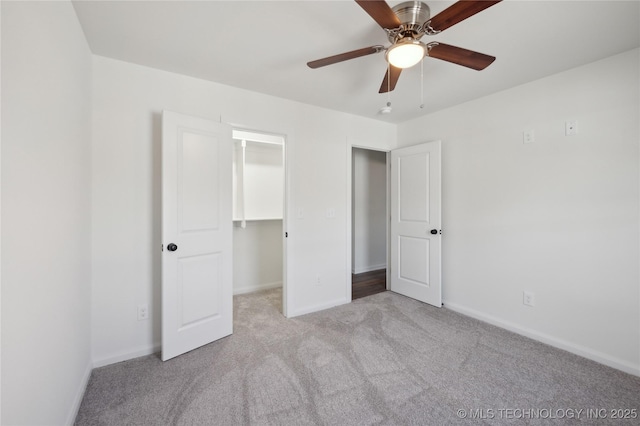 unfurnished bedroom featuring a walk in closet, carpet floors, baseboards, and a ceiling fan