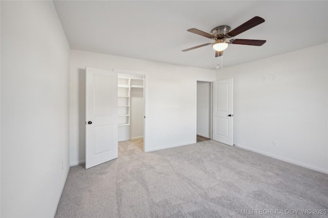 unfurnished bedroom featuring baseboards, a spacious closet, ceiling fan, and carpet flooring