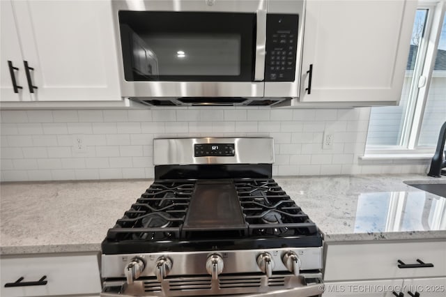 kitchen with backsplash, white cabinets, stainless steel appliances, and light stone counters